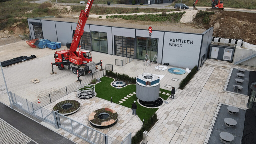 Roter Mobilkran hebt rundes Lüftungsmodul im Innenhof vor dem Gebäude "Venticer World", Techniker beobachten